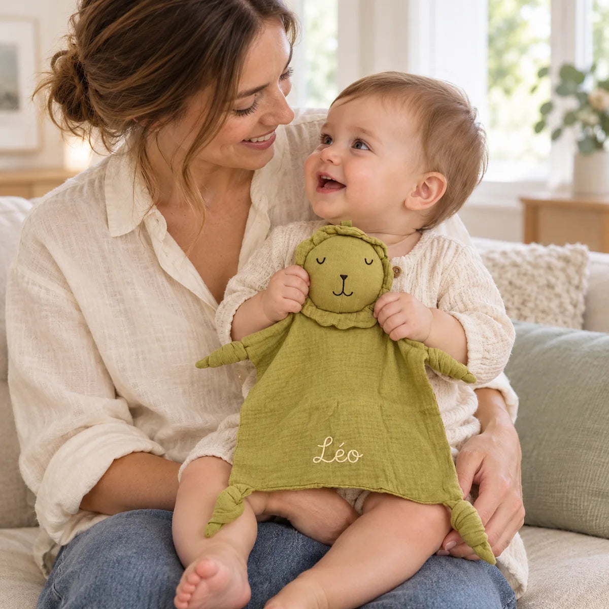 Bébé éveillé sur les genoux de sa maman découvrant le doudou lion vert olive brodé Léo
