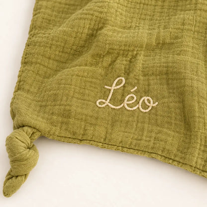 Gros plan sur le prénom Léo brodé en fil clair et le tissu vert olive du doudou lion