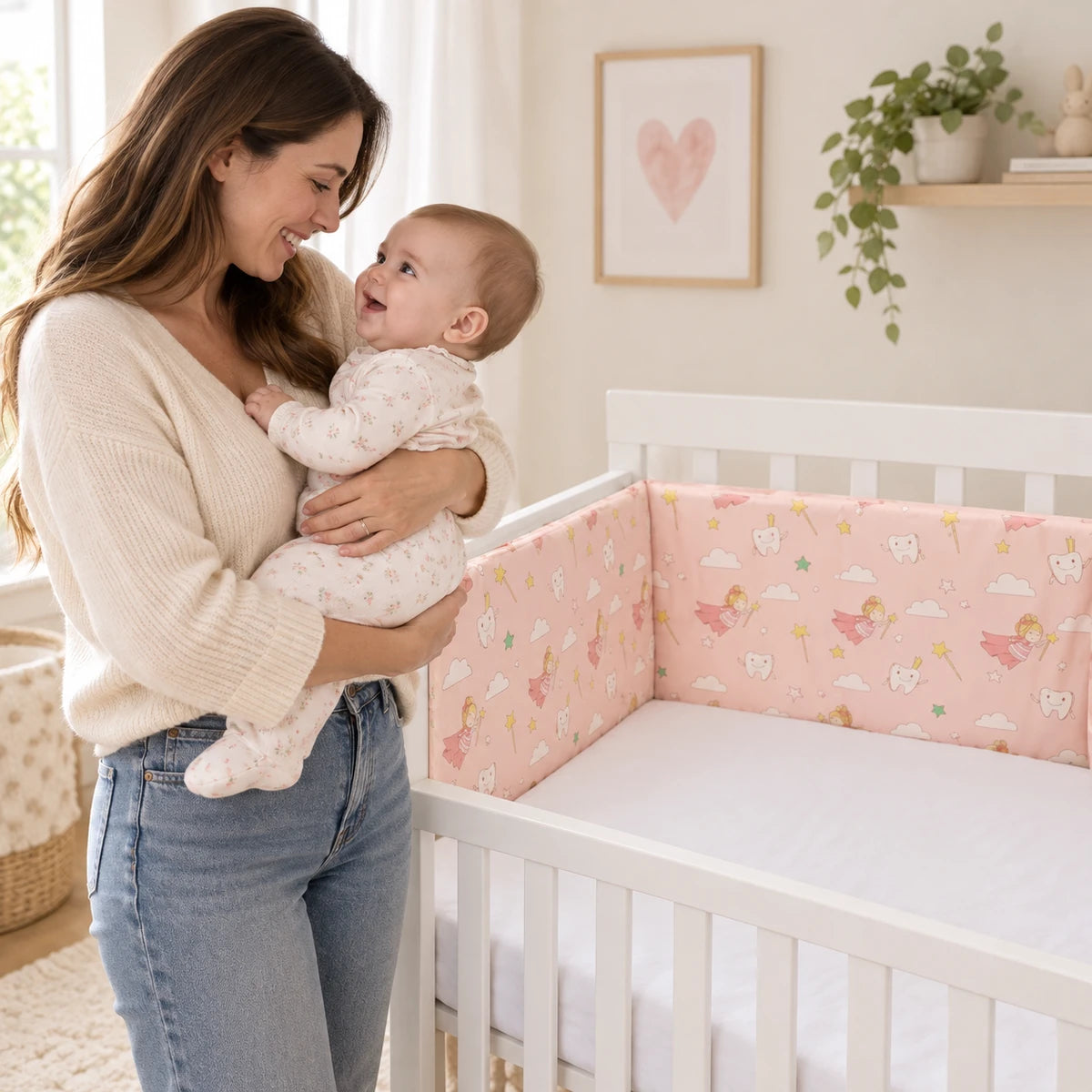 Maman tenant son bébé éveillé à côté du lit vide décoré avec le tour de lit Féerie Rose.
