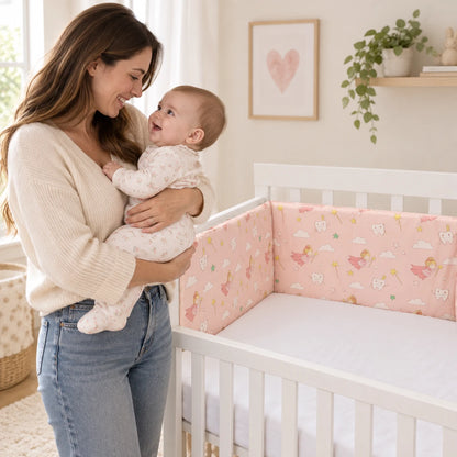 Maman tenant son bébé éveillé à côté du lit vide décoré avec le tour de lit Féerie Rose.