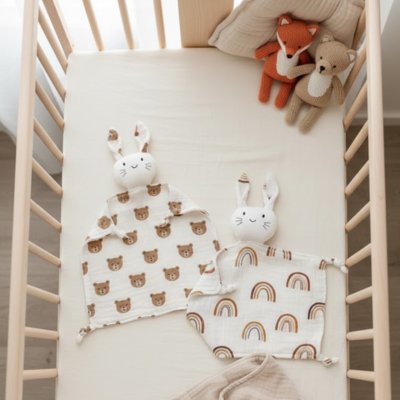 Doudou lapin avec motif ourson et arc en ciel posés sur lit bébé