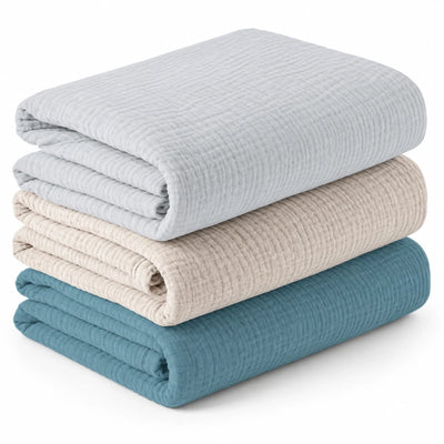 Lot de trois couvertures bébé unies pliées, gris perle, beige et bleu.
