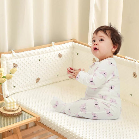 un bébé qui jour sur son lit protégé par le tour de lit
