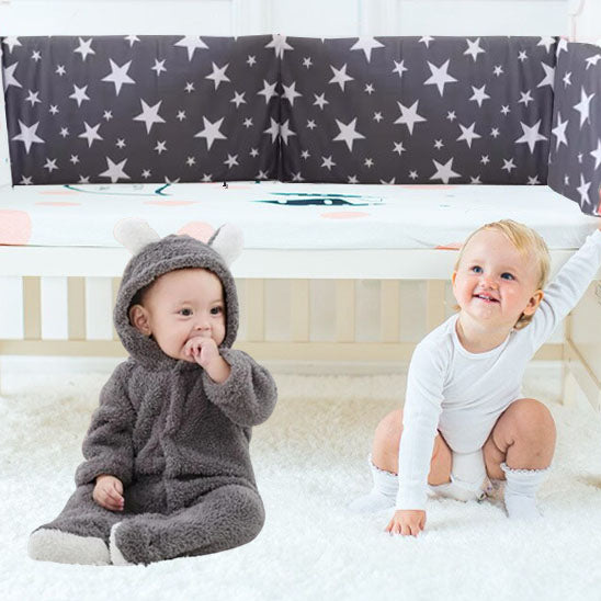 Deux bébés mignons qui jouent à côté du lit couvert d'un tour de lit 