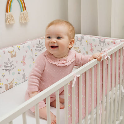 une jolie petite fille qui rigole dans son lit protégé par un tour de lit bébé