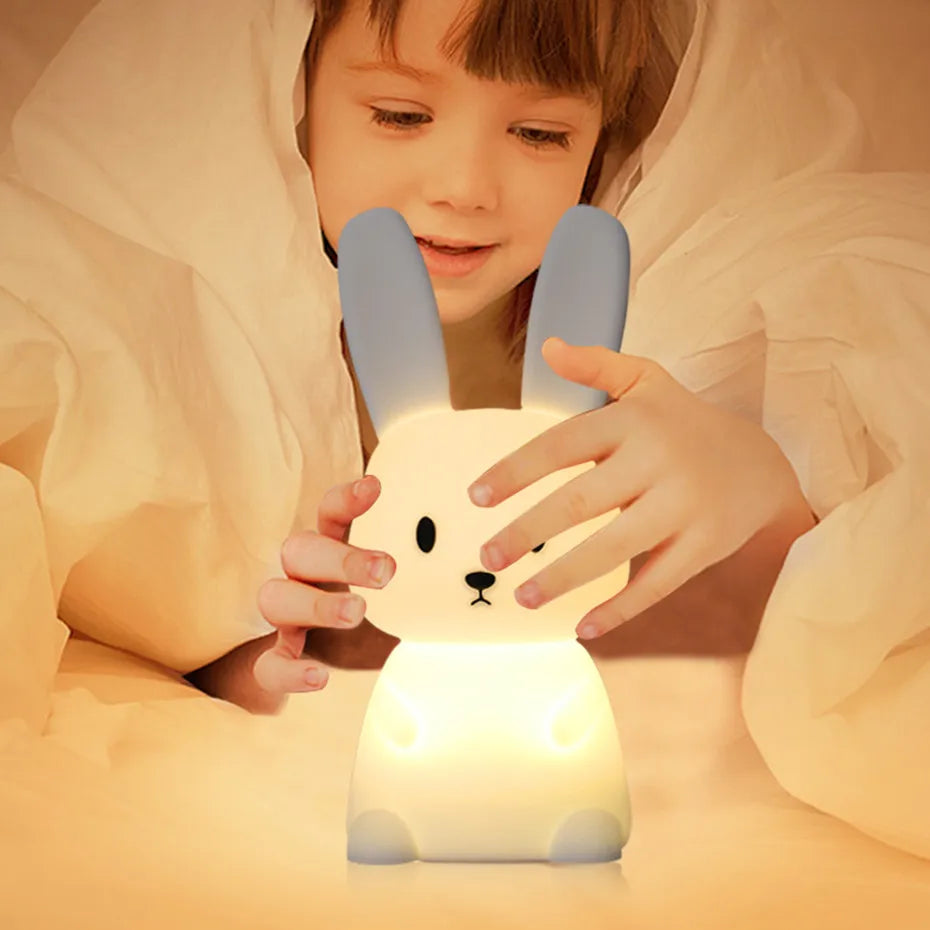 Un garçon qui s'apprête à dormir joue avec sa veilleuse lapin Lapinou couvert sous les draps