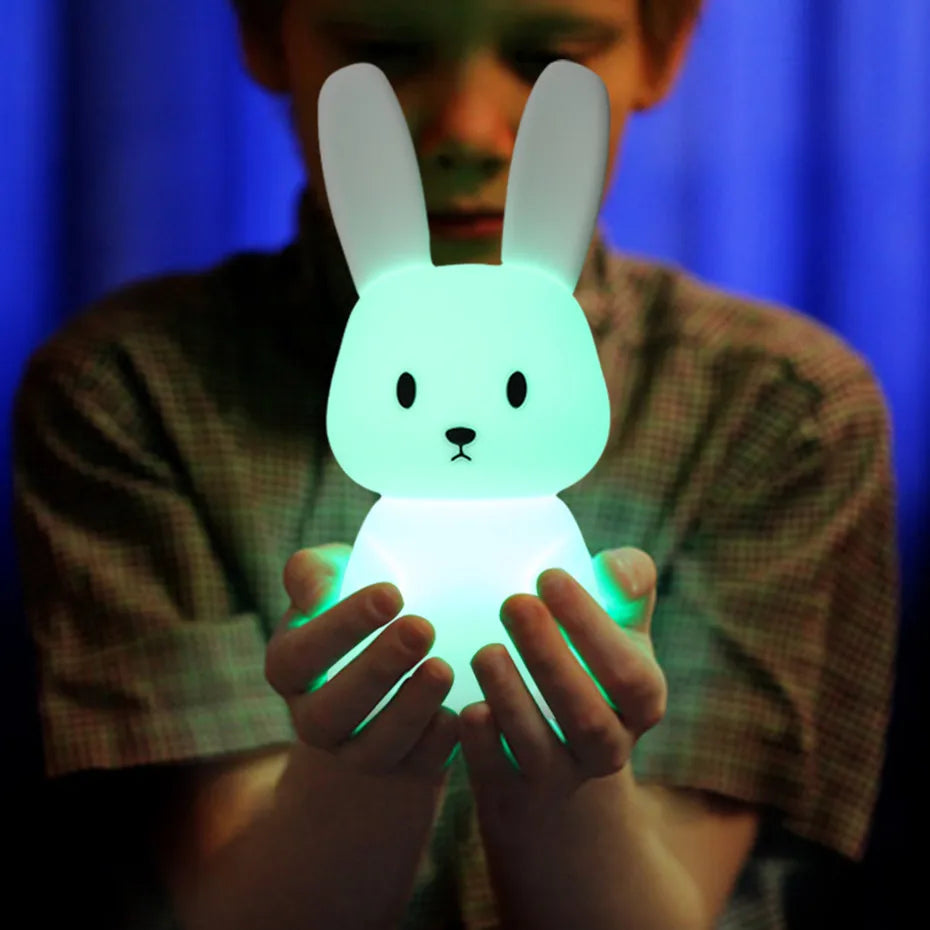 Un garçon qui tient avec deux mains la veilleuse lapin avec lumière verte apaisante